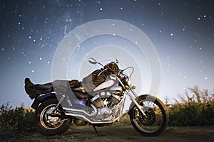 Young beautiful biker woman with motorcycle under stars of our home galaxy Miky Way. Female biker on field at night