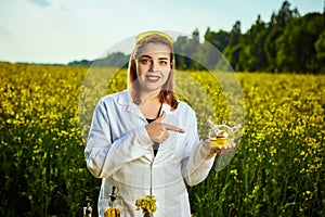 A young beautiful biologist or agronomist examines the quality of rapeseed oil on a rape field. Agribusiness concept