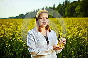 A young beautiful biologist or agronomist examines the quality of rapeseed oil on a rape field. Agribusiness concept