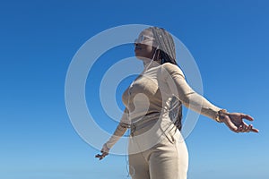 Young beautiful black afro girl with open arms, blue sky background, attitude and inspiration, motivation, positivity