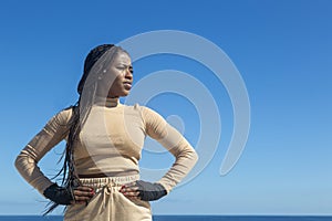 Young beautiful black afro girl prepared to train with hands on waist and background of sea and blue sky, attitude and