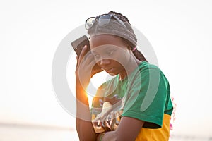 Young beautiful black girl using smart phone on sea beach at sunset
