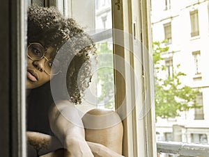 Young beautiful black pensive woman sitting near the window in a nostalgic mood