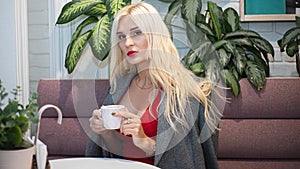 Young beautiful blond woman in an autumn coat seets in the cafe. Soft focus. Fashionable concept