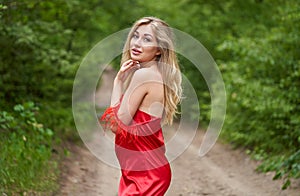 Young, beautiful blond woman with bright make-up and with long hair in a red dress effectively posing on the road in the park