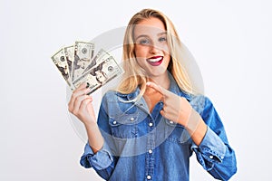 Young beautiful blond woman holding dollars standing over isolated white background very happy pointing with hand and finger