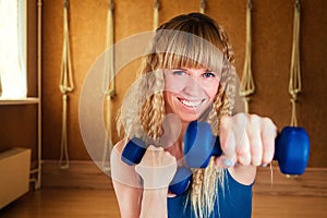 Young and beautiful blond woman is holding dumbbells in the hands of a gym. The yoga instructor performs respiratory