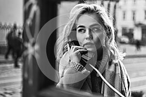 Young beautiful blond woman making an important call in a vintage public phone booth on a sunny evening