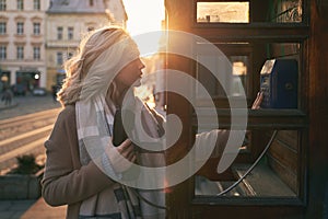 Young beautiful blond woman ready to make an important call in a vintage public phone booth on a sunny evening