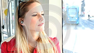 Young beautiful blond woman riding tram, listening to music and dancing