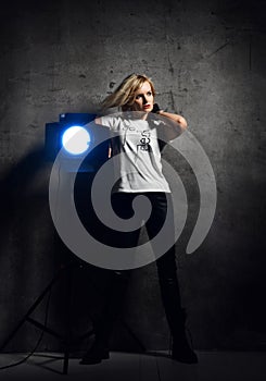 Young beautiful blond woman in stylish casual clothing and black boots standing near light fixture