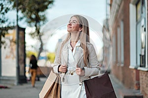 Young beautiful blond woman is walking along a city street from a store. Carries a lot of shopping bags in her hands.