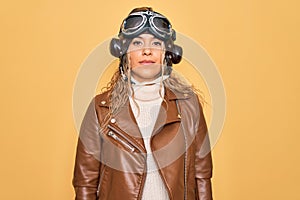 Young beautiful blonde aviator woman wearing vintage pilot helmet whit glasses and jacket Relaxed with serious expression on face