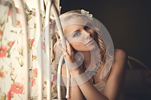 Young beautiful blonde in the bed at morning time near window under Sun rays with flower in the hair. Tender romantic mood