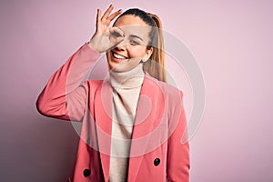 Young beautiful blonde businesswoman with blue eyes wearing elegant pink jacket doing ok gesture with hand smiling, eye looking