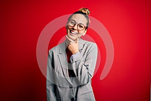 Young beautiful blonde businesswoman with blue eyes wearing glasses and jacket looking confident at the camera smiling with