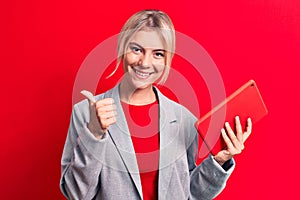 Young beautiful blonde businesswoman working using tablet over isolated red background smiling happy and positive, thumb up doing