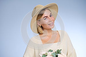 A young beautiful blonde caucasian woman with a short haircut in a beige suit and hat with bouquet of white flowers on