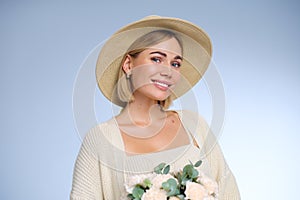 A young beautiful blonde caucasian woman with a short haircut in a beige suit and hat with bouquet of white flowers on