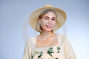 A young beautiful blonde caucasian woman with a short haircut in a beige suit and hat with bouquet of white flowers on