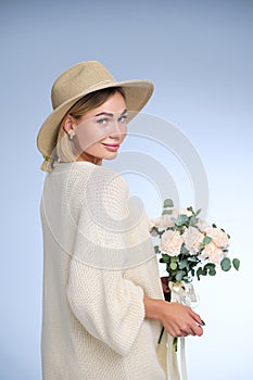 A young beautiful blonde caucasian woman with a short haircut in a beige suit and hat with bouquet of white flowers on