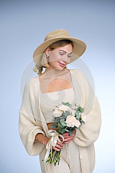 A young beautiful blonde caucasian woman with a short haircut in a beige suit and hat with bouquet of white flowers on