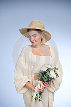 A young beautiful blonde caucasian woman with a short haircut in a beige suit and hat with bouquet of white flowers on