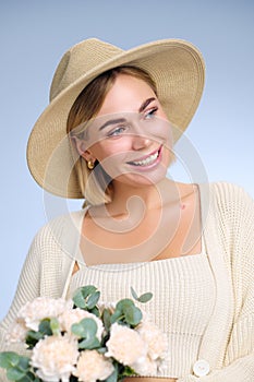 A young beautiful blonde caucasian woman with a short haircut in a beige suit and hat with bouquet of white flowers on