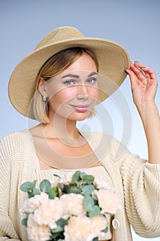 A young beautiful blonde caucasian woman with a short haircut in a beige suit and hat with bouquet of white flowers on