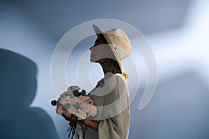 A young beautiful blonde caucasian woman with a short haircut in a beige suit and hat with bouquet of white flowers on