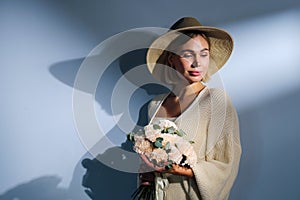 A young beautiful blonde caucasian woman with a short haircut in a beige suit and hat with bouquet of white flowers on