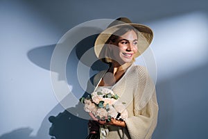 A young beautiful blonde caucasian woman with a short haircut in a beige suit and hat with bouquet of white flowers on