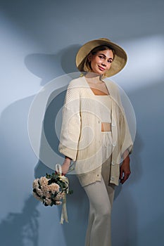 A young beautiful blonde caucasian woman with a short haircut in a beige suit and hat with bouquet of white flowers on