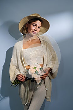 A young beautiful blonde caucasian woman with a short haircut in a beige suit and hat with bouquet of white flowers on