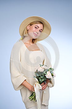 A young beautiful blonde caucasian woman with a short haircut in a beige suit and hat with bouquet of white flowers on