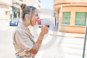 Young beautiful blonde caucasian woman smiling happy outdoors on a sunny day shouting through megaphone