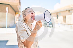 Young beautiful blonde caucasian woman smiling happy outdoors on a sunny day shouting through megaphone