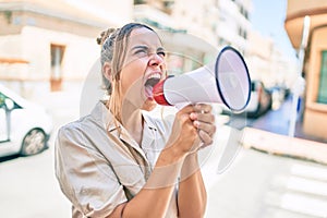 Young beautiful blonde caucasian woman smiling happy outdoors on a sunny day shouting through megaphone