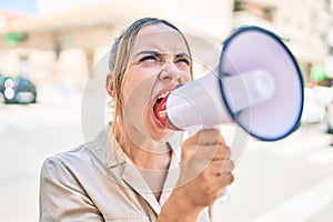 Young beautiful blonde caucasian woman smiling happy outdoors on a sunny day shouting through megaphone