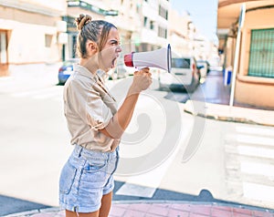 Young beautiful blonde caucasian woman smiling happy outdoors on a sunny day shouting through megaphone