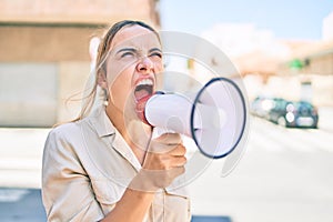 Young beautiful blonde caucasian woman smiling happy outdoors on a sunny day shouting through megaphone