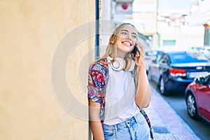 Young beautiful blonde caucasian woman smiling happy outdoors on a sunny day wearing headphones and using smartphone