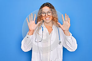 Young beautiful blonde doctor woman with blue eyes wearing coat and stethoscope showing and pointing up with fingers number ten