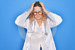 Young beautiful blonde doctor woman with blue eyes wearing coat and stethoscope suffering from headache desperate and stressed