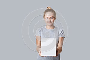 Young beautiful blonde female with hair bun holds white box in hands, with copy space for your text, isolated over grey background