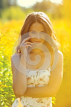 Young beautiful blonde in a field with yellow flowers. One hand to the face