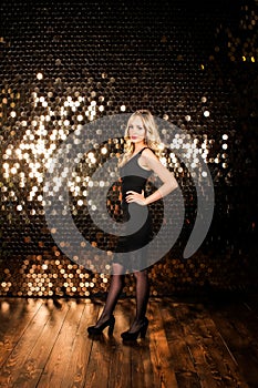Young beautiful blonde girl in a black evening dress on the background of shiny golden wall