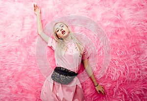 Young beautiful blonde girl dressed in fashion pink dress poses on the background of pink fur wall in the show room