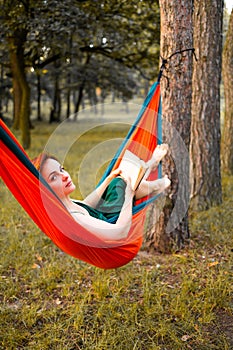 Young blonde girl in hammock reading book. Pretty woman leisure lifestyle at nature ountdoor. Female relax in forest.