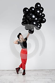 Young beautiful blonde girl holding black baloons over white wall.